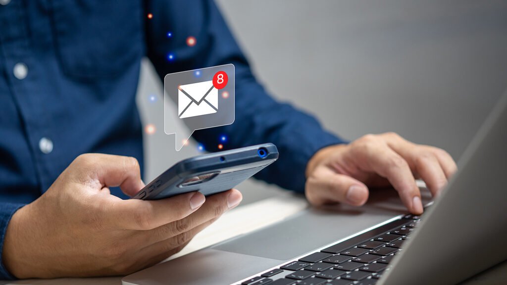 Person checking email on phone and laptop, with an email notification showing eight unread messages.