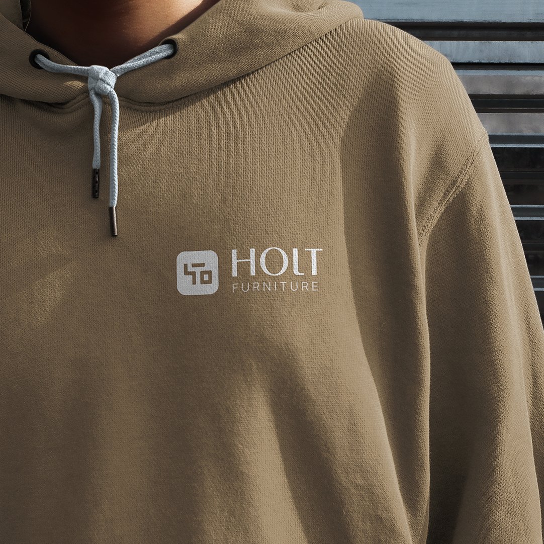 Close-up of a person wearing a tan hoodie with the white "HOLT FURNITURE