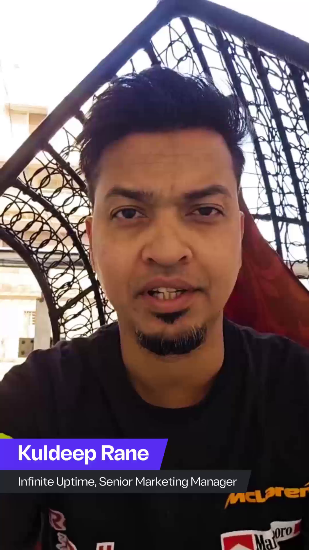 Close-up of Kuldeep Rane, Senior Marketing Manager at Infinite Uptime, speaking outdoors while seated in a hanging chair. He is wearing a black t-shirt with McLaren branding, and a text overlay displays his name and title.
