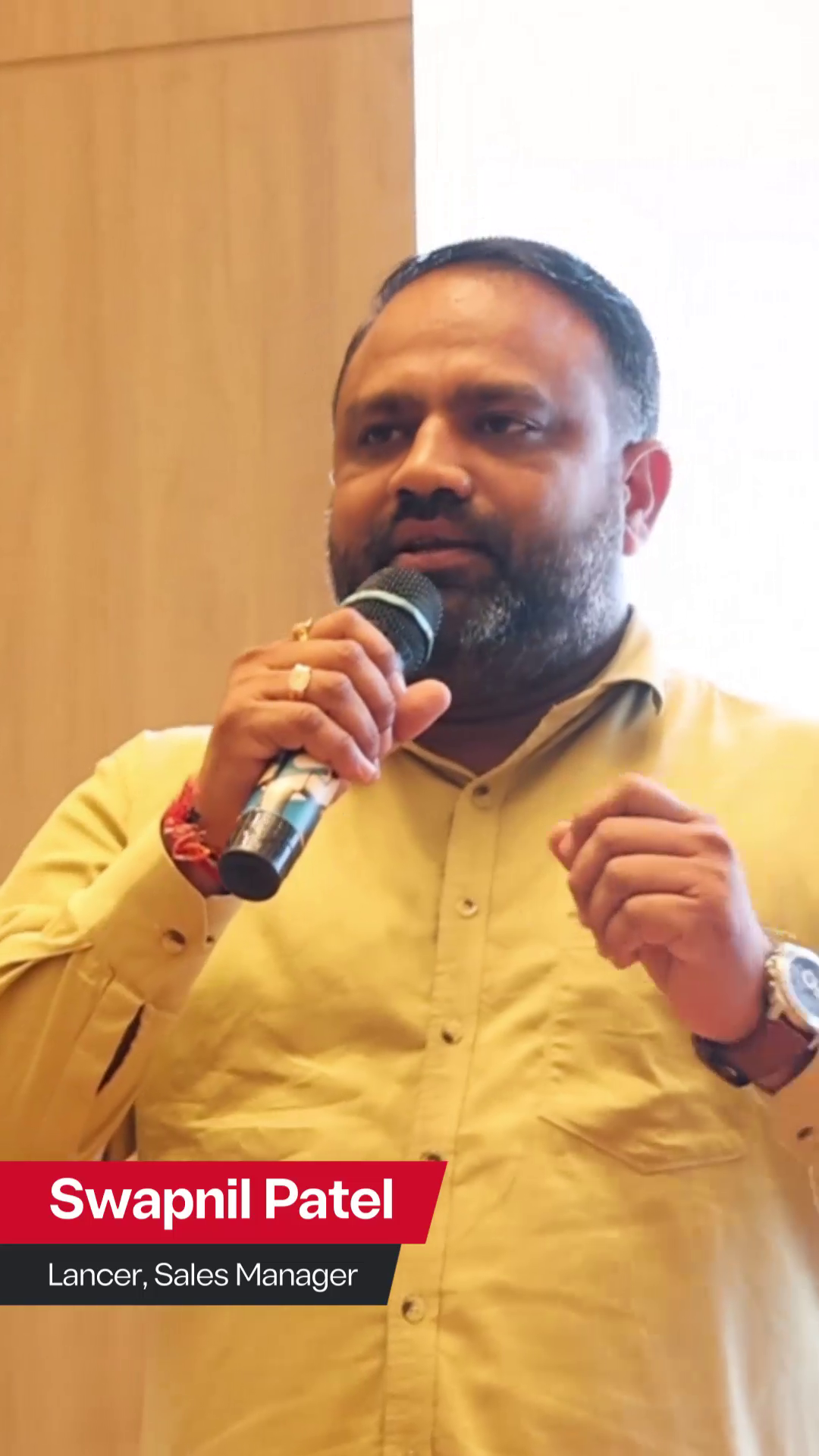 Swapnil Patel, Sales Manager at Lancer, speaking into a microphone during a presentation. He is wearing a yellow shirt and gesturing with his hand, with a red and black text overlay displaying his name and title.