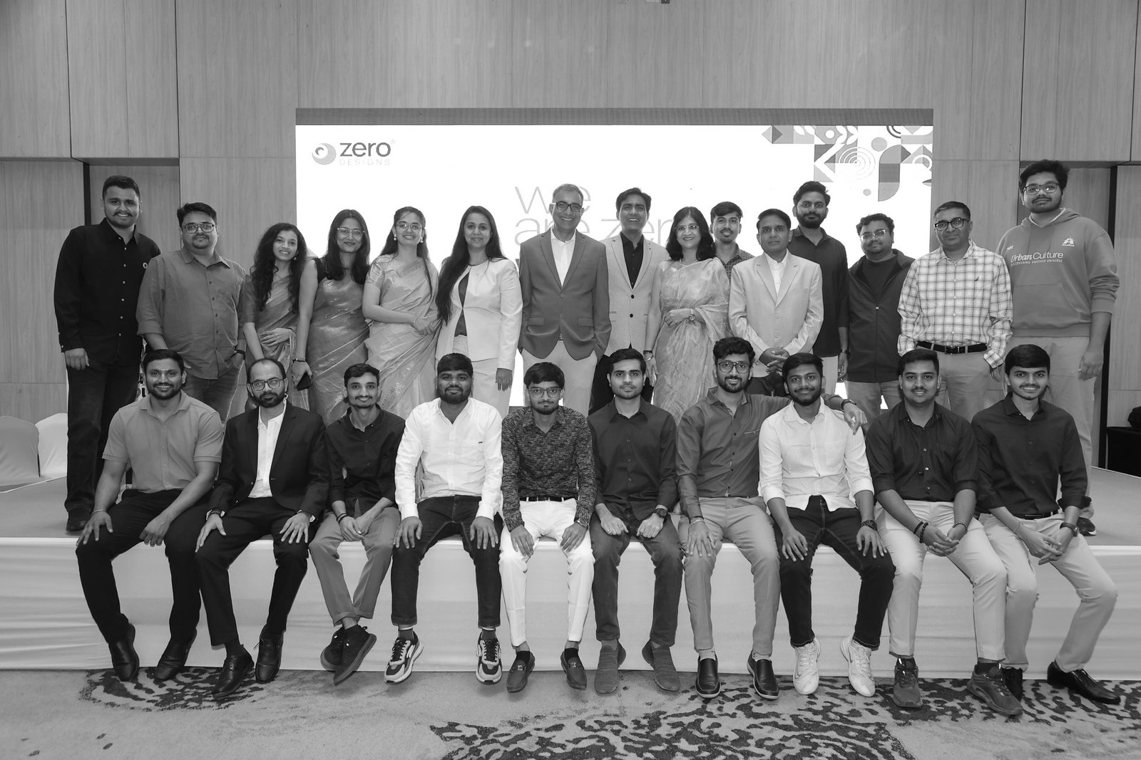 Group photo of the entire Zero Designs team, posing together on stage in front of a branded backdrop during an event, in black and white.